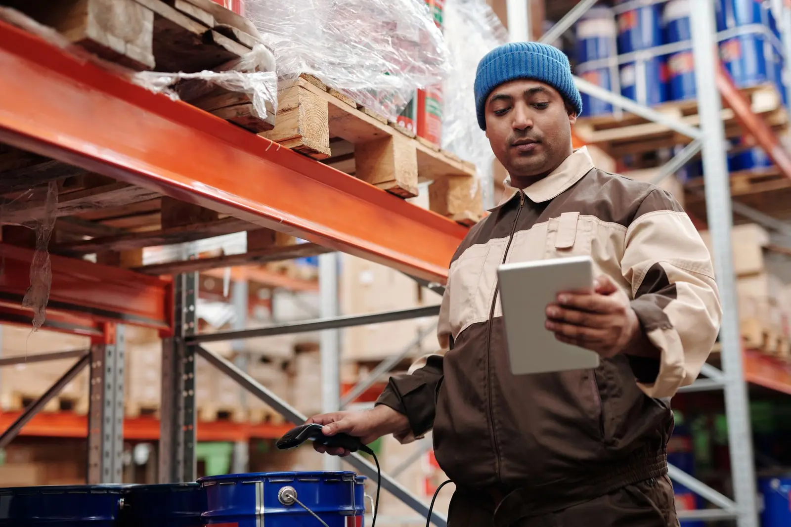 Mitarbeiter in Arbeitsjacke prüft am Tablet Bestände vor orangefarbenen Regalen, Symbolbild